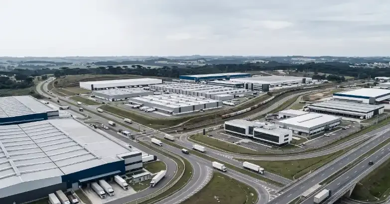 Vista aérea de um complexo industrial com galpões e pátios, cercado por rodovias e vias de acesso, em área rural no horizonte